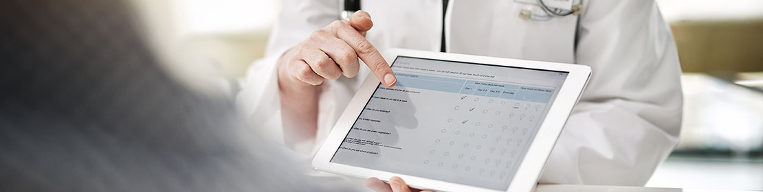Doctor holds a tablet and points at an online form.